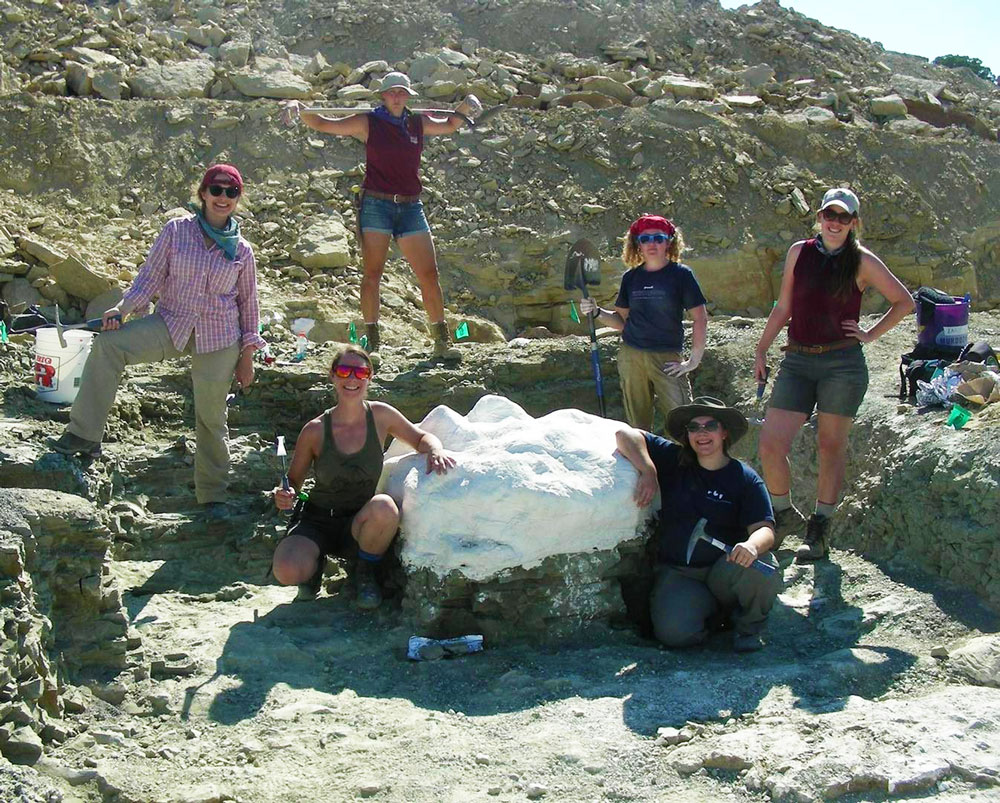 The 2021 paleo team posing in front of a field jacket at the Jurassic Mile dig site in Wyoming.
